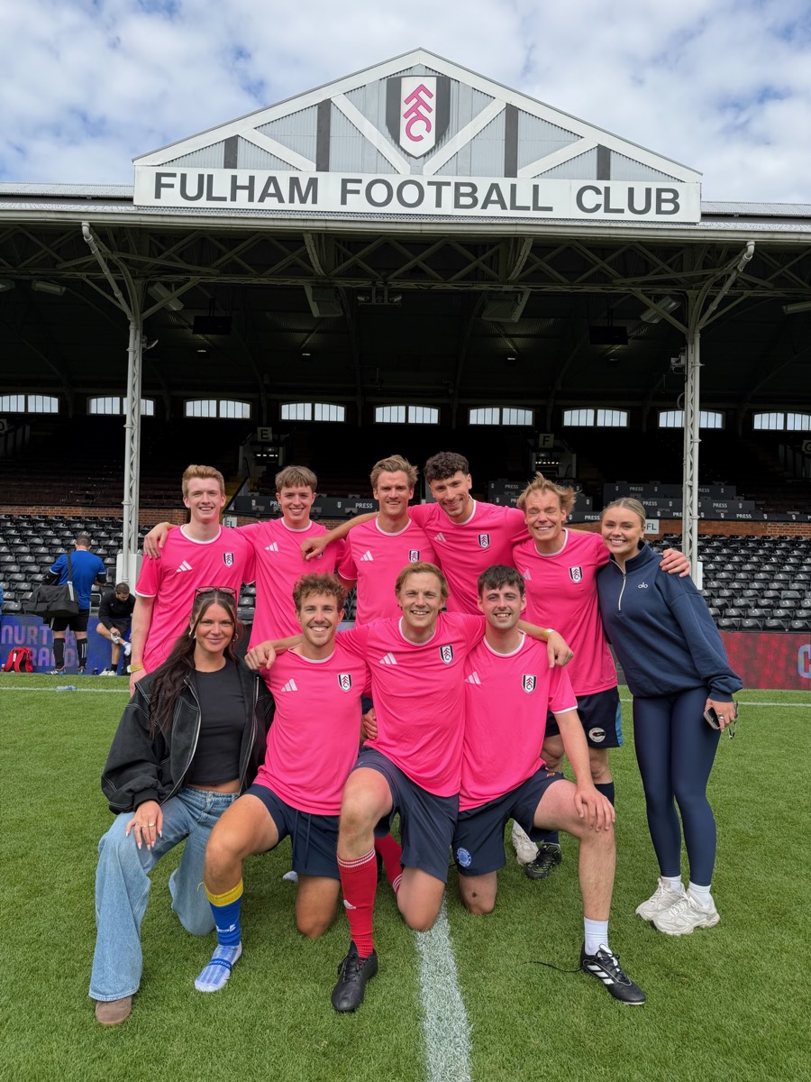 Team REMAKER in pink Fulham shirts on the pitch at Craven Cottage, under the Fulham Football Club sign